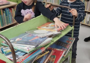 Dziewczynka z chłopcem przyciągnęli wózek do zbierania książek.