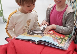 Dziewczynka z chłopcem siedzą na pufie i ogladają książkę.