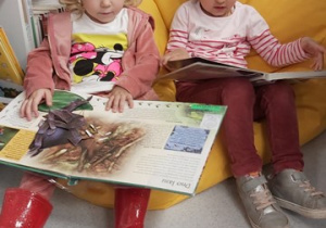 Dwie dziewczynki siedzą na pufie i ogladają książki o zwierzętach.