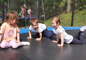 Troje dzieci skacze na trampolinie.