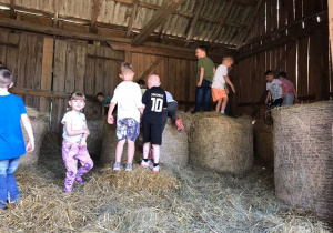 Dzieci skaczą po sianie w stodole.