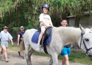 Chłopiec siedzi na koniu,który jest prowadzony przez opiekuna.