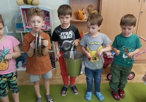Pięcioro dzieci gra na kuchennych akcesoriach: przykrywki do garnka, wiadro, łyżki.