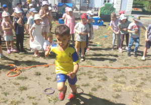 Dzieci biorą udział w zabawach sportowych, Chłopiec biegnie pomiędzy kółkami.
