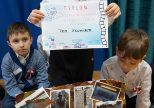 Chłopiec pokazuje swoją pracę na konkurs o Warszawie oraz otrzymany dyplom.