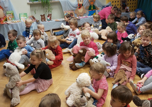 Dzieci siedzą na podłodze i trzymają swoje ulubione misie.