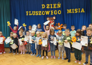 Dzieci z dyplomami za udział w konkursie plastycznym "Ekologiczny Miś" .W tle widać napis "Dzień Pluszowego Misia".
