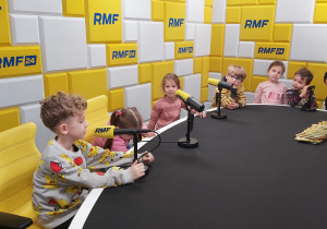 dzieci siedzą przy stole z mikrofonami z napisami RMF FM.