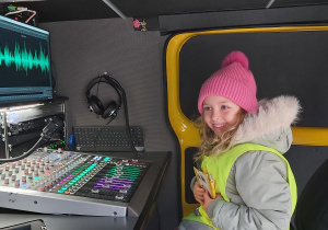 Dziewczynka stoi przy pulpicie redakcyjnym w wozie transmisyjnym RFM FM.