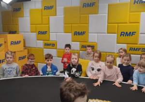 Dzieci siedzą przy stole na tle ścianki z napisami RMF FM.