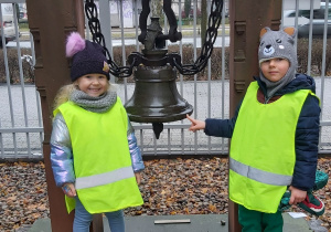 Dziewczynka i chłopiec stoją obok dzwonu.
