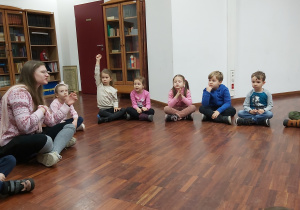 Dzieci siedzą na podłodze i uczestniczą w warsztach "Zabawy azjatyckie".