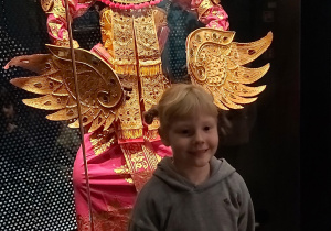 Dziewczynka stoi na tle manekina ubranego w azjatycki regionalny strój.