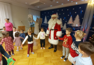 Dzieci tańczą w kole razem z Mikołajem.
