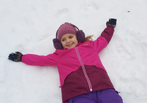 Dziewczynka leży na śniegu i robi "aniołki".