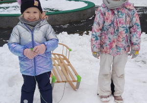 Dwie dziewczynki stoją na śniegu i trzymają sanki.