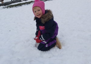Dziewczynka klęczy na śniegu i lepi kulki.