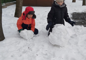 Dwóch chłopców lepiśniegowe kule, turlając je po śniegu.