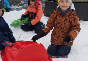 Chłopcy bawią się na śniegu plastikowymi sankami i klockami.
