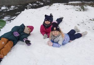 Trzy dziewczynki leżą na śniegu.
