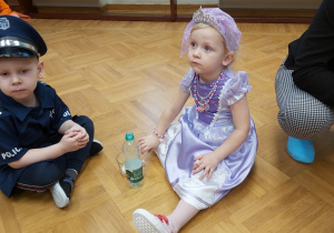 Dziewczynka przebrana za królewnę oraz chłopiec przebrany za policjanta biorą udział w konkursie- zbierają ziarenka fasoli do butelki.