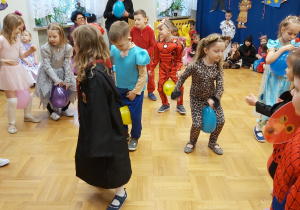 Dzieci z najstarszej grupy tańczą w kole z balonami między kolanami.