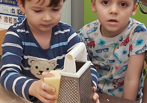 Dwóch chłopców ściera na tarce ser żółty.