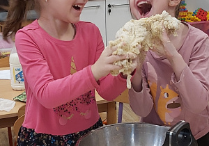 Dwie uśmiechnięte dziewczynki trzymają w rękach przygotowane ciasto na pizzę.
