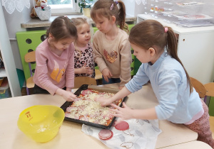 Cztery dziewczynki posypują pizzę utartym serem.