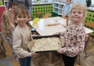 Dwie dziewczynki pokazują przygotowaną do pieczenia pizzę.