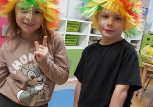 Dziewczynka z chłopcem pozują w kolorowych perukach.