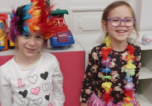 Dwie dziewczynki w przebraniach. jedna ma na głowie kolorową perukę, druga zaś hawajskie kwiaty i kolorową spódnicę z pasków.