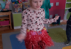 Dziewczynka ubrana w biało-czerwoną perukę oraz czerwoną spódnicę z pasków tańczy.