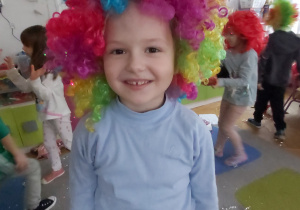 Uśmiechnięta dziewczynka pozuje do zdjęcia w kolorowej peruce.