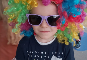 Chłopiec pozuje do zdjęcia w kolorowej peruce i okularach przeciwsłonecznych..