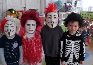 Czworo dzieci pozuje w kolorowych perukach oraz w maskach na twarzy.