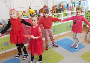 Dzieci ubrane na czerwono tworzą koło. W środku stoi dziewczynka trzymająca serduszko.