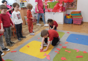 Dzieci dobierają pasujące do siebie części serca, które są rozsypane na dywanie.