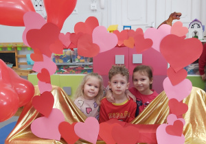 Dwie dziewczynki i chłopiec pozują do zdjęcia w fotoramce ozdobionej sercami .