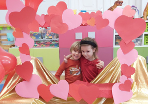 Dziewczynka i chłopiec pozują do zdjęcia w fotoramce ozdobionej sercami .