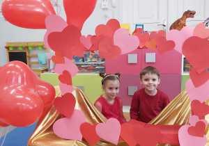 Dziewczynka i chłopiec pozują do zdjęcia w fotoramce ozdobionej sercami .