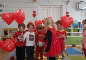 Dzieci stoją w grupie. W rękach trzymają balony w kształcie serca.