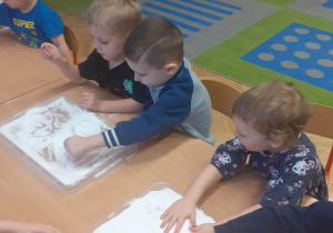 Dzieci rysują palcem w soli rozsypanej w tackach.
