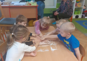 Dzieci odbijają swoje dłonie w soli na tackach.
