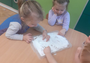Dziewczynka i chłopiec rysują palcem obrazki w soli na tacce.
