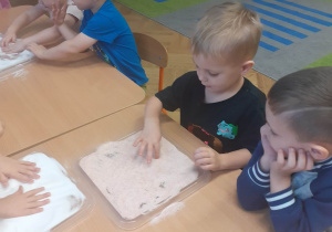 Dzieci rysują palcem obrazki w soli na tacce.