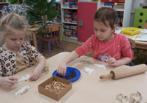 Dwie dziewczynki siedzą przy stoliku i z masy plastycznej wycinają dinozaury za pomocą foremek.