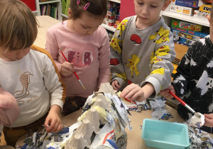 Dzieci wykonują sylwetę dinozaura doklejając kawałki gazet.