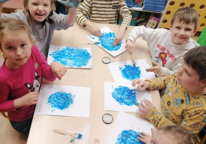 Dzieci rozmazują plastikowymi widelcami plamy z niebieskej farby .