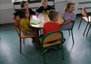 Dzieci siedzą przy stoliku w szkolnej bibliotece.